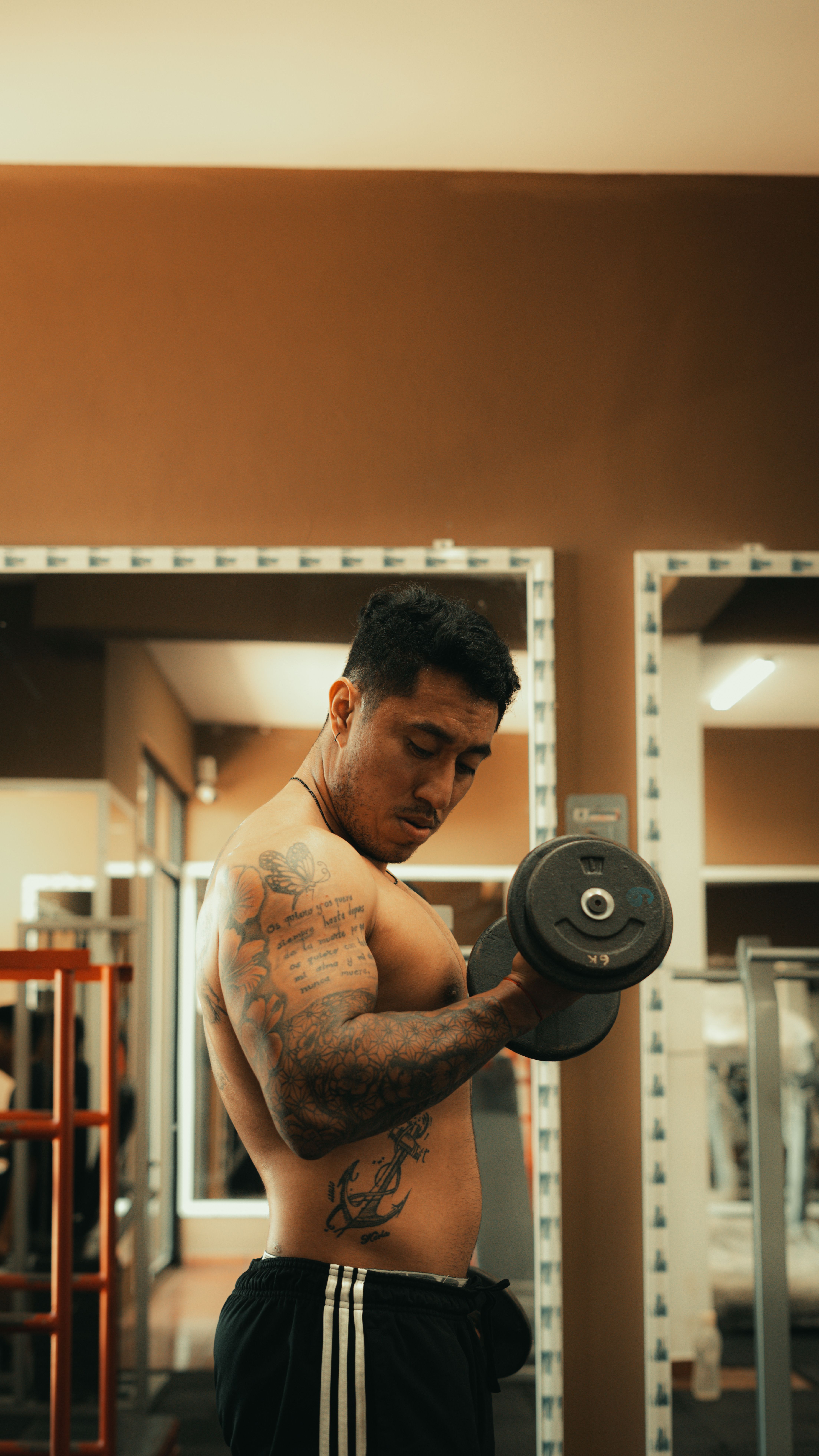 Strong tattooed man lifting a dumbbell in a gym, showcasing focus and fitness.