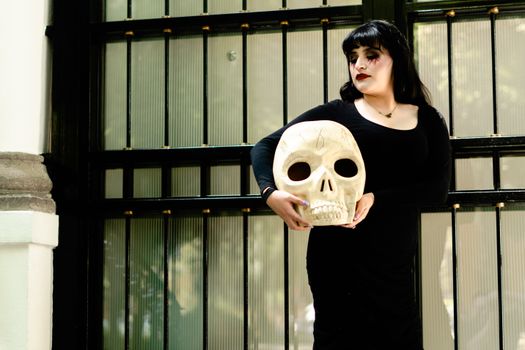 A woman in black dress holds a skull, celebrating tradition near a historical building in Mexico City.