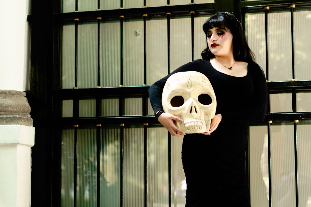 a woman in black dress holds a skull celebrating tradition near a hist