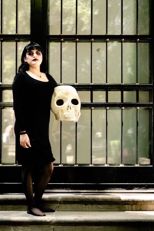 Woman in a Black Dress and Wearing Halloween Makeup Holding a Skull 