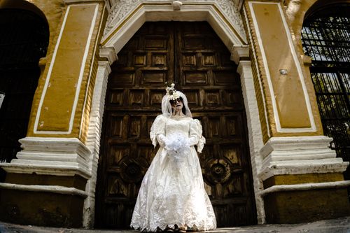 Free A woman in Catrina makeup and wedding dress stands elegantly before a rustic door in Ciudad de México. Stock Photo