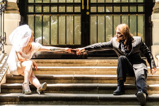 A couple in Halloween costumes reaching out on stone steps in daylight.