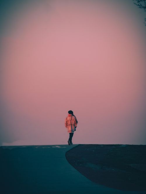 Free A solitary figure walks along a road silhouetted against a pink dusk sky, creating a peaceful scene. Stock Photo