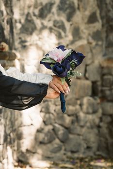 Close-up of a bridal bouquet held against a rustic stone wall with soft lighting.