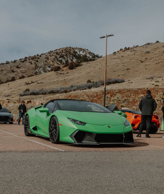 A striking green Lamborghini Huracan parked outdoors with hills in the background and several people nearby.