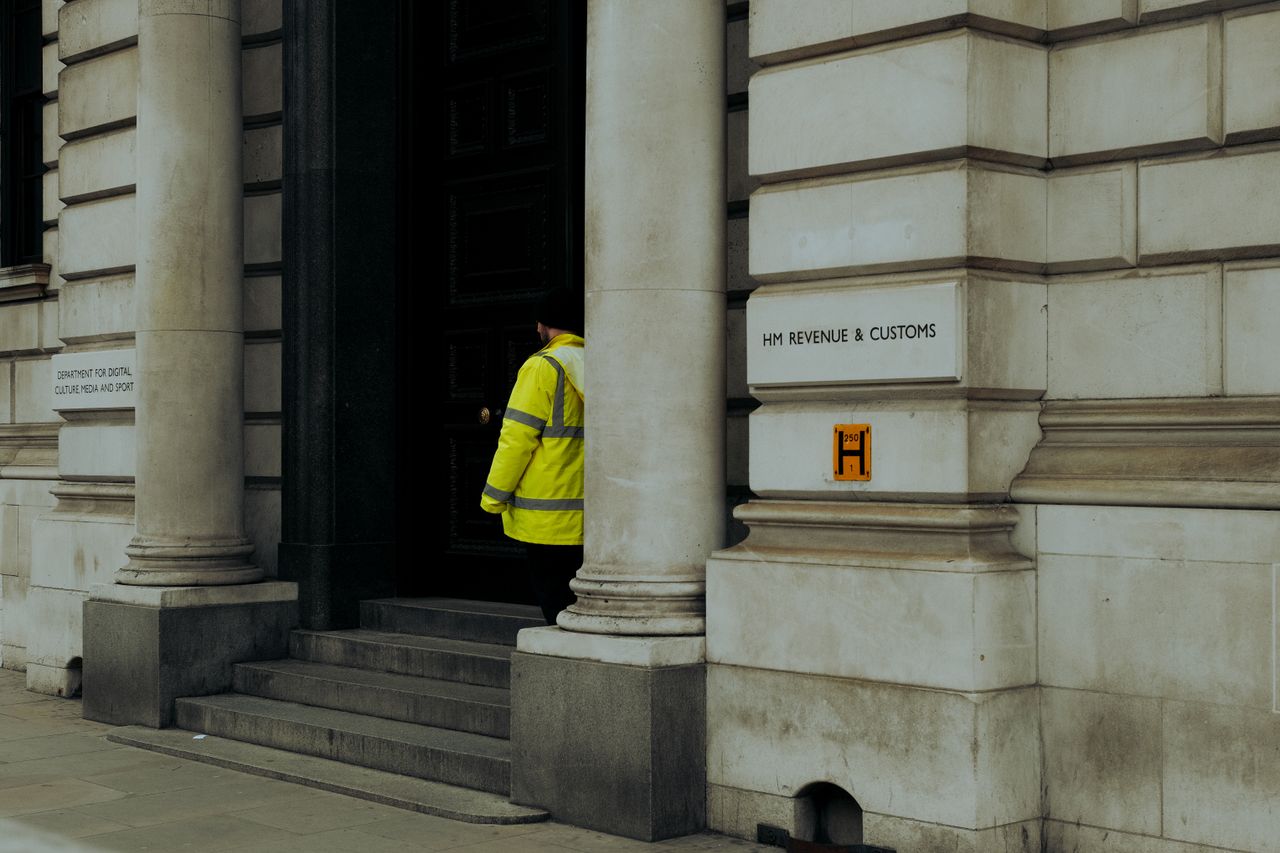 A guard in yellow jacket at the entrance of HM Revenue & Customs building in the UK.