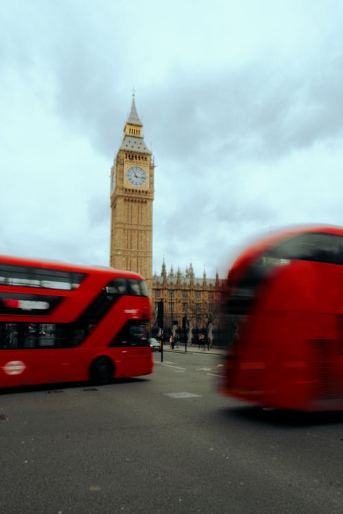 Free Red double-decker buses in motion near Big Ben under an overcast sky in London, UK. Stock Photo