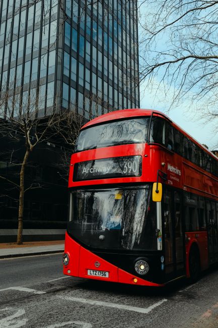 Red double-decker bus passing a city street in London with modern architecture.