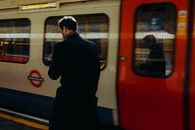 Man walks past a moving train on a London Underground platform during the day.