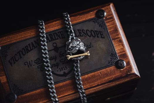 Close-up of a Cuban link chain featuring a detailed pendant, set on a wooden Victorian marine telescope box.