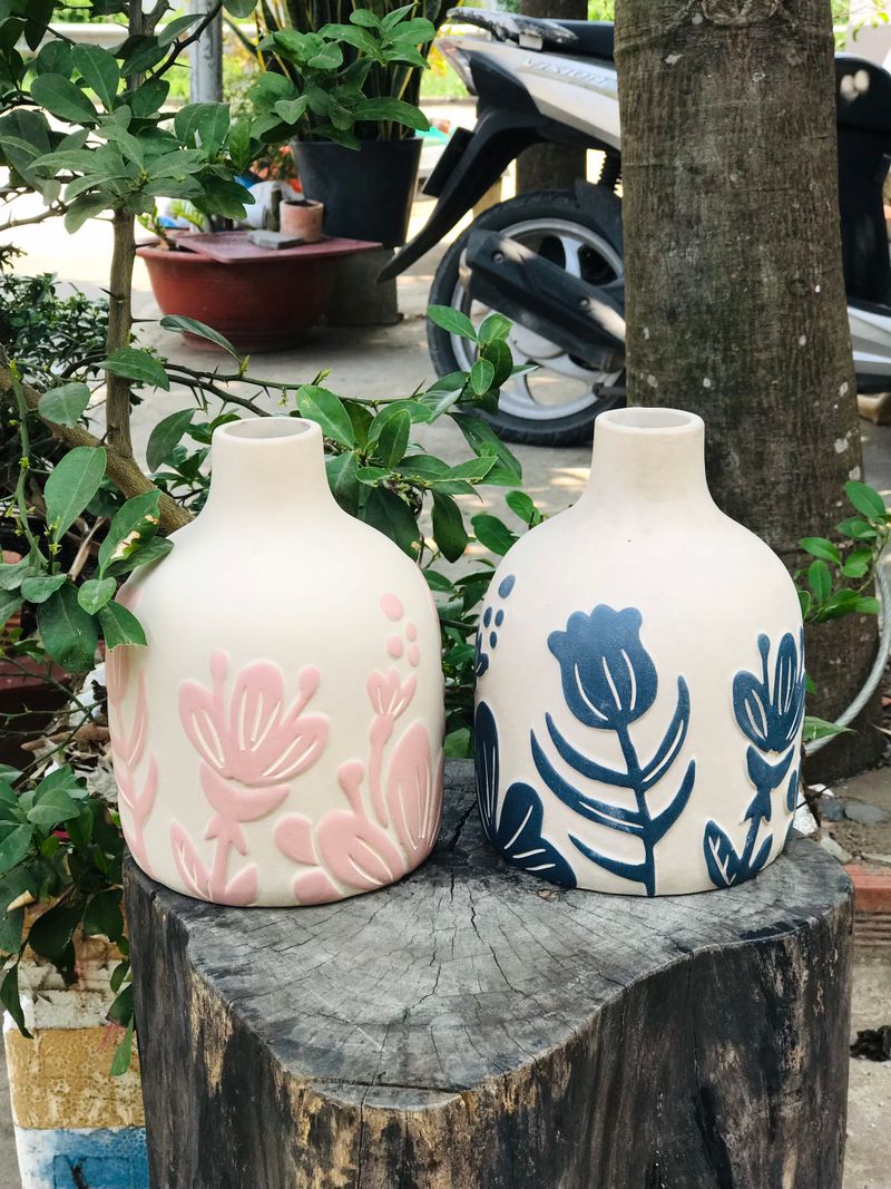 Two white vases painted with pink and blue flowers on a tree stump