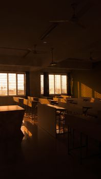 Warm light fills an empty classroom, highlighting desks at sunset.