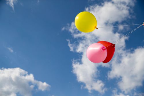 Free Bright yellow, pink, and red balloons float against a clear blue sky, celebrating summer joy. Stock Photo