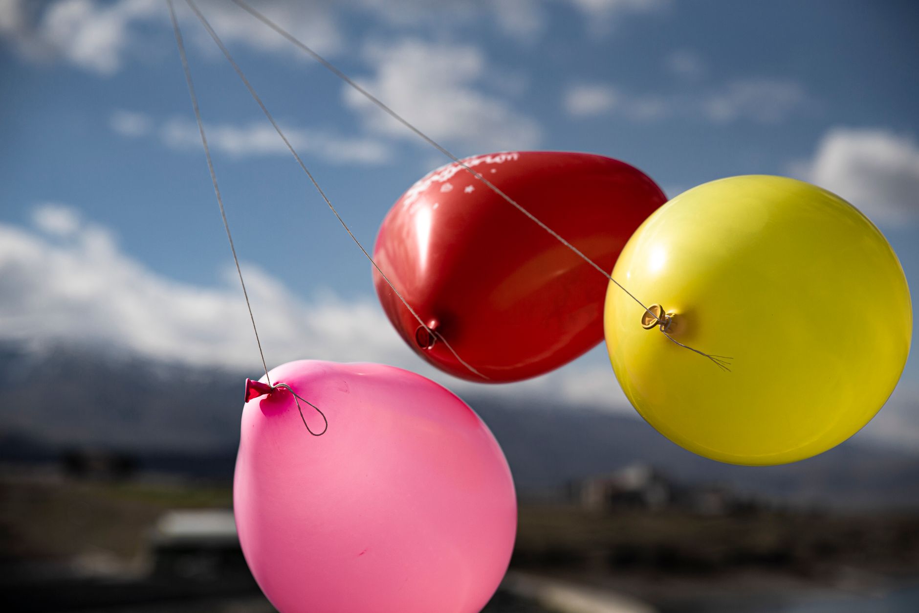 Three colorful balloons float against a bright blue sky, symbolizing celebration.