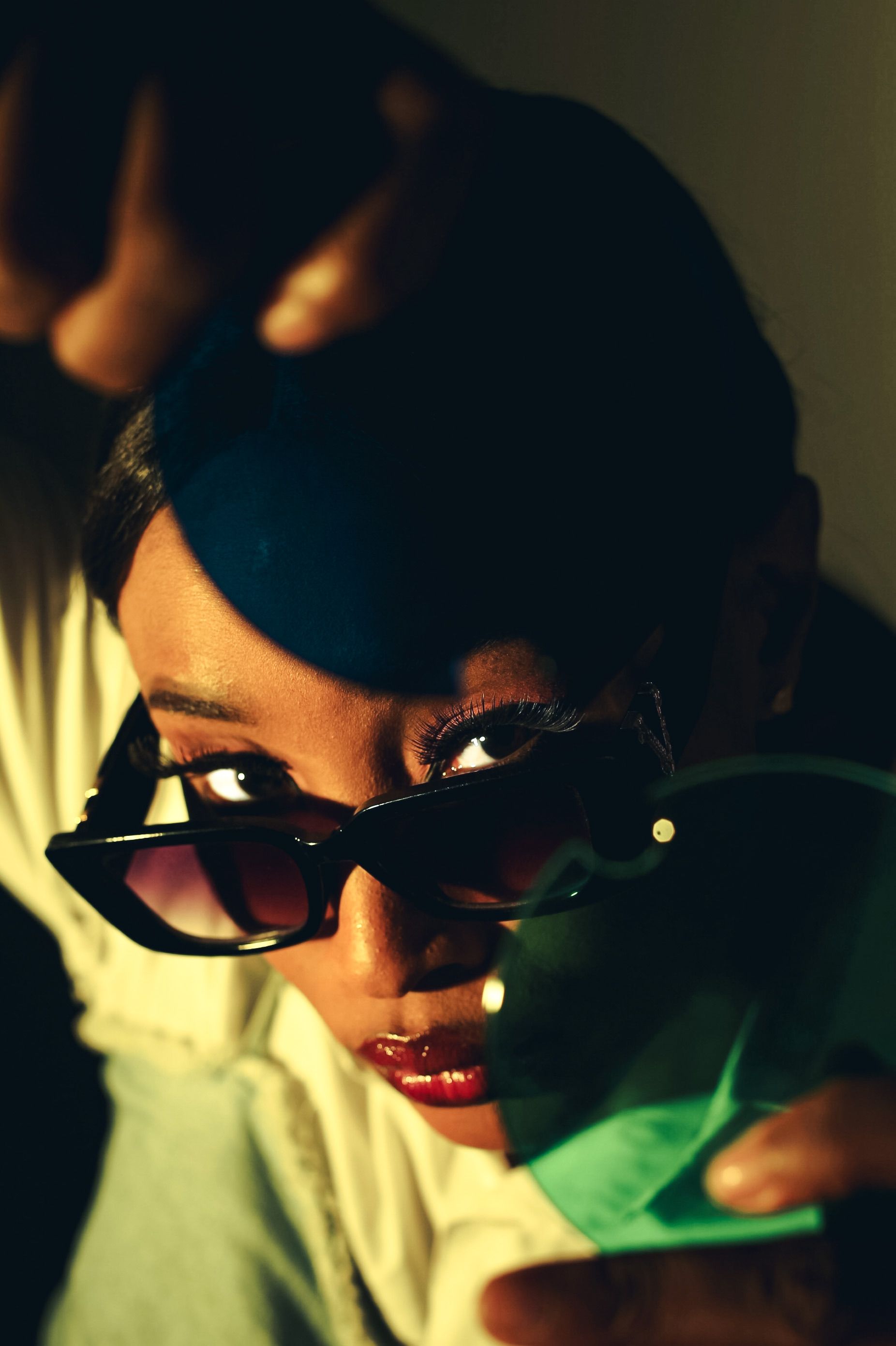 Artistic portrait of a woman wearing sunglasses, posing dramatically under warm lighting.