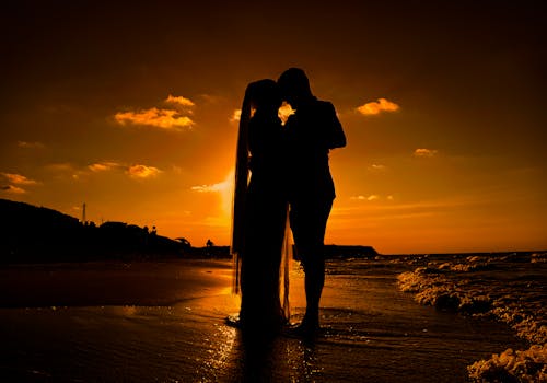 Silhouetted Couple Standing on a Beach at Sunset and Hugging 