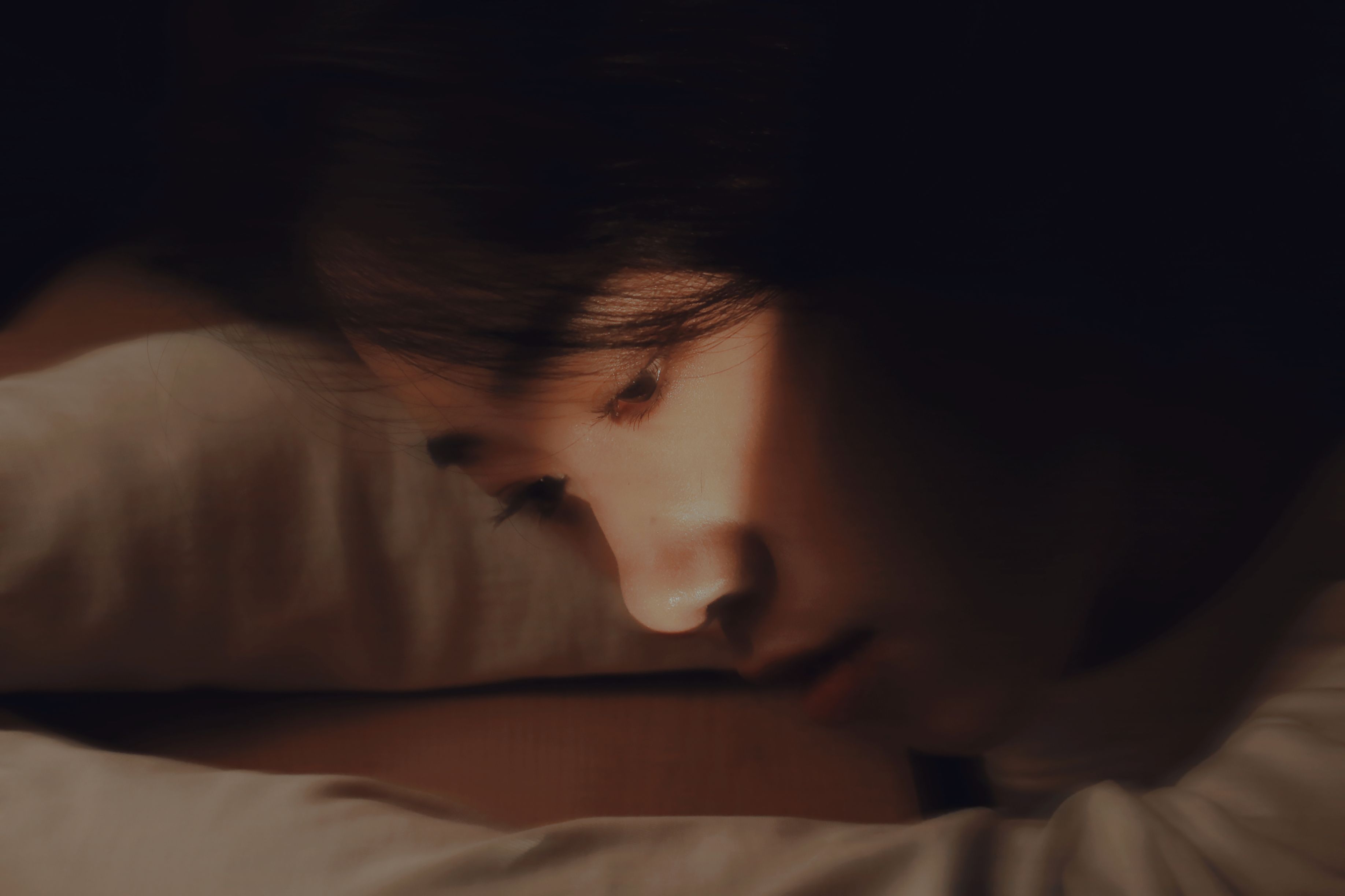 A woman rests her head on a desk, deep in thought with moody lighting.