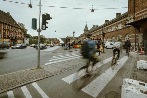 Free Cyclists ride through a bustling urban intersection in a European city with historical architecture. Stock Photo