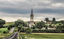 天空多云，郁郁葱葱的田野中矗立着教堂和风车，风景如画