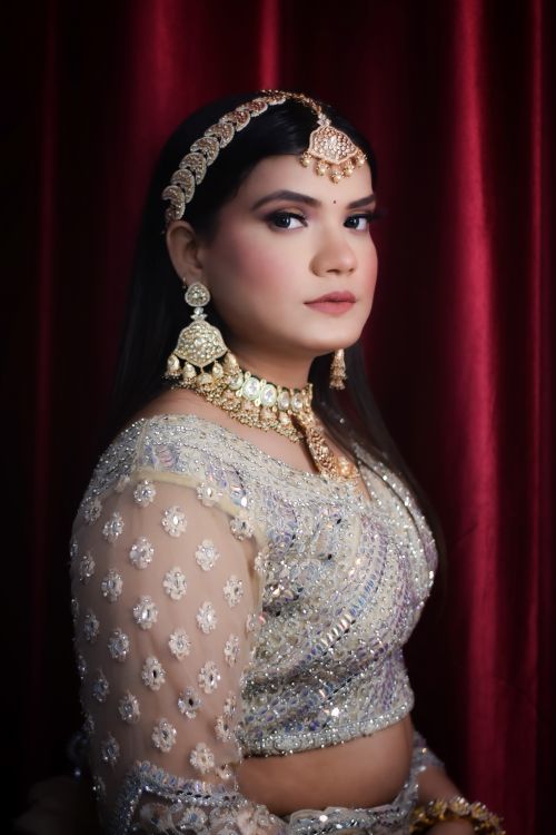 Free Portrait of an Indian woman in traditional attire, adorned with gold jewelry against a rich red backdrop. Stock Photo