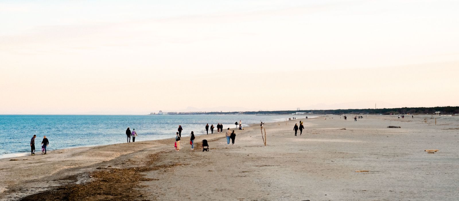 Tranquil beach scene at Marina di Ravenna with people walking along the shoreline.