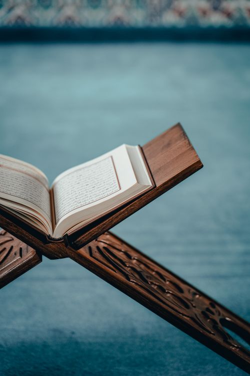 Free An open Quran displayed on an intricately designed wooden stand, evoking spiritual tranquility. Stock Photo