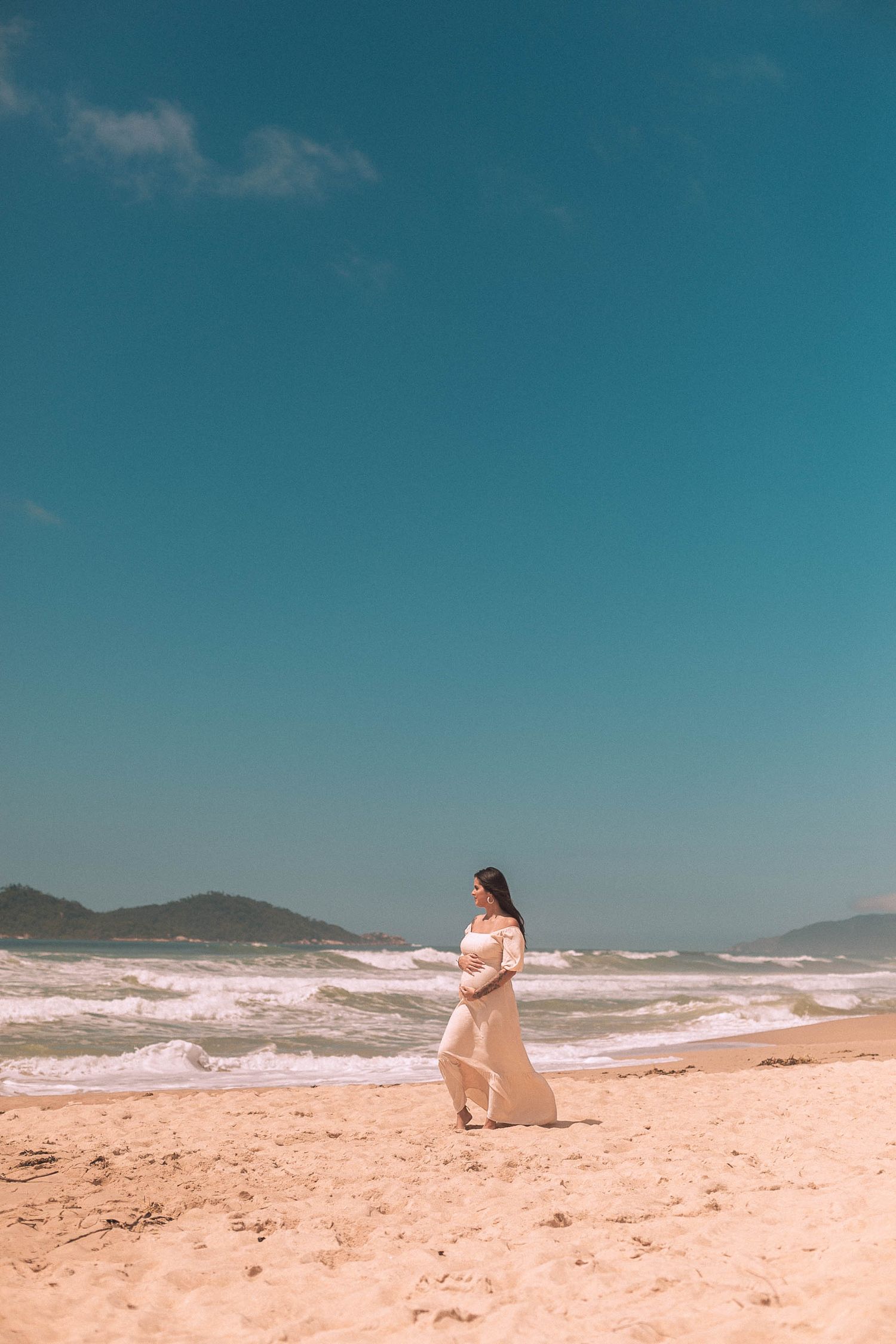 Future maman en robe blanche marchant au bord de la mer pendant une journée d’été