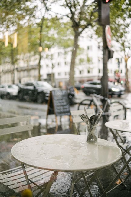 A wet table with cutlery at a Paris sidewalk cafe on a rainy day.