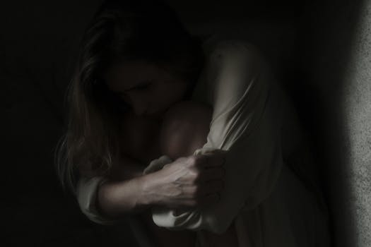 A woman sits in a dimly lit corner, evoking feelings of solitude and introspection.