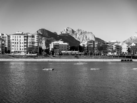 A scenic black and white cityscape featuring urban buildings along a waterfront with mountains in the background.