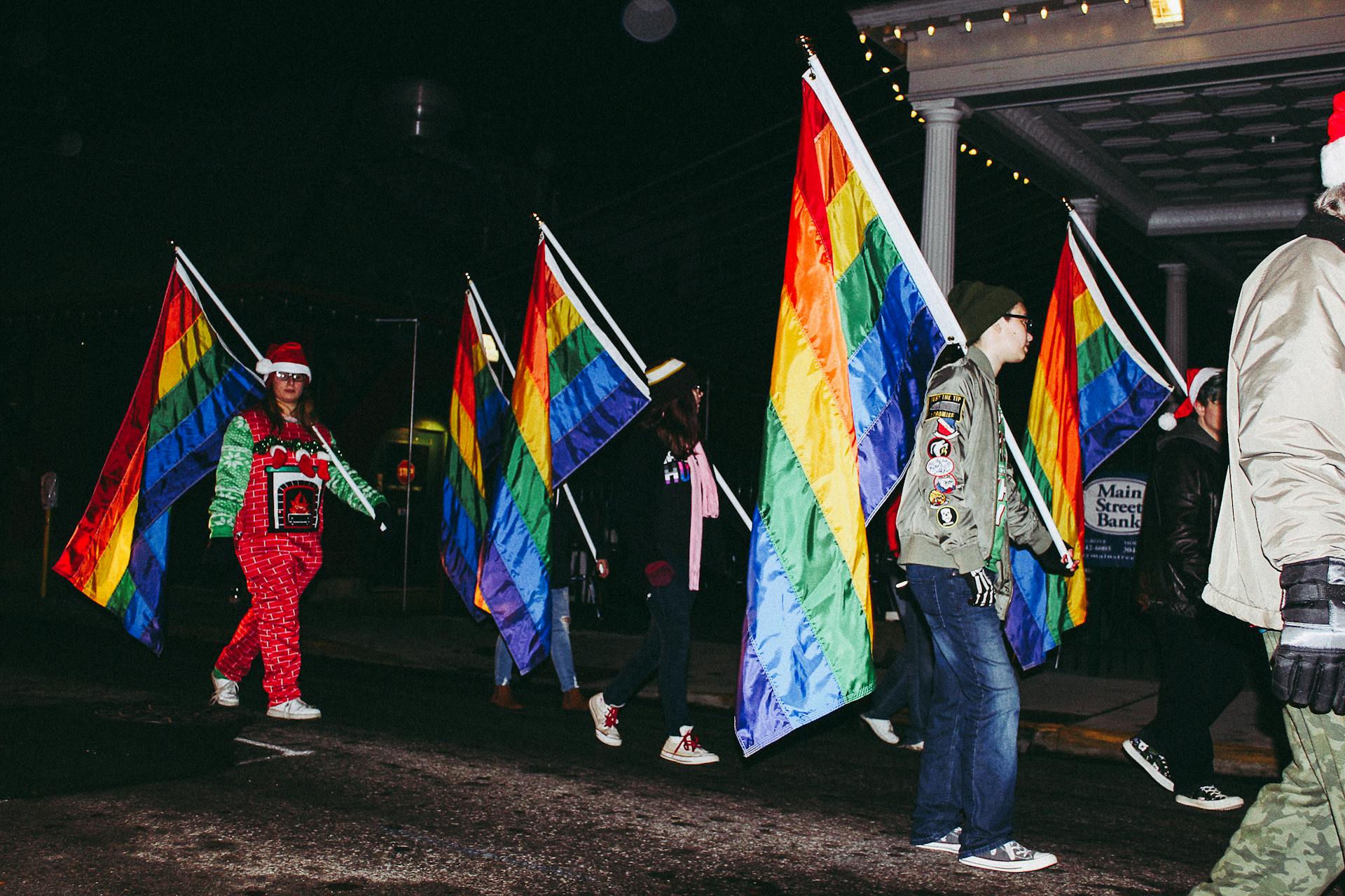 A colorful pride parade with people marching at night, holding rainbow flags and expressing joy.