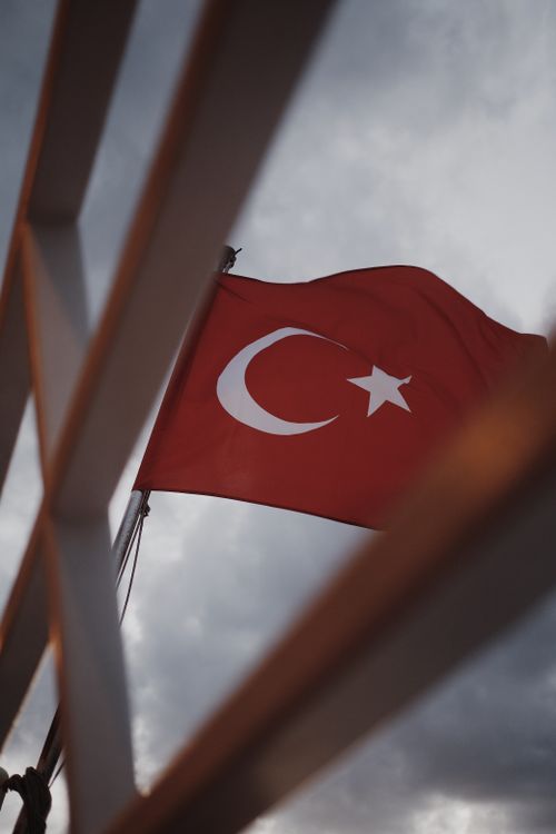 Free Red Turkish flag captured with a low angle and cloudy sky, framed by railings. Stock Photo