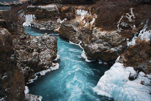 Captivating winter scene of an icy river with vivid blue waters meandering through a rocky gorge in Iceland.