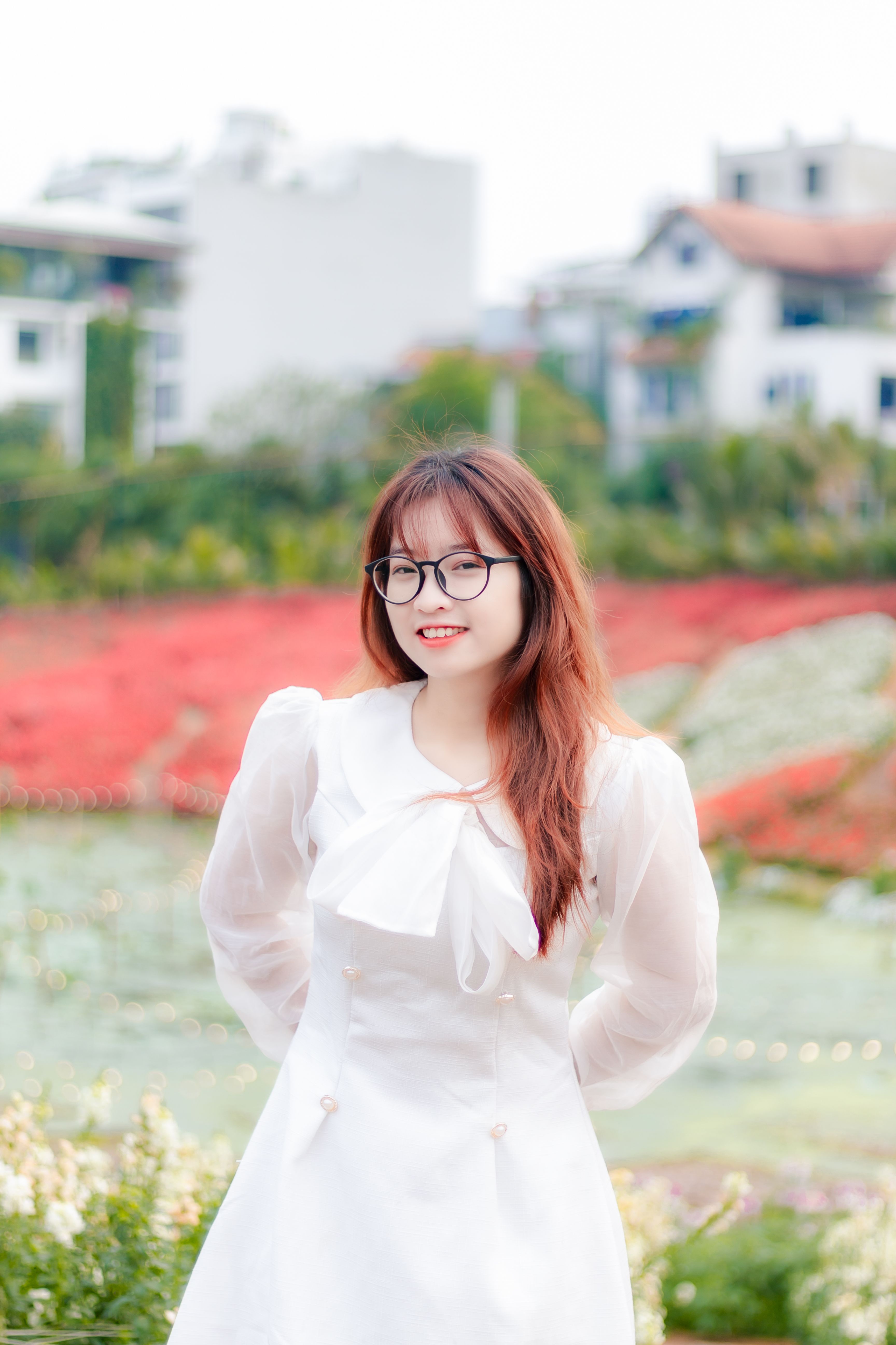 Smiling young woman in a white dress posing outdoors with a colorful blurred background.