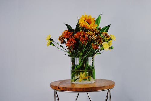 Flores De Pétalos De Color Naranja, Rojo Y Amarillo En Un Jarrón De Vidrio Transparente Sobre Una Mesa Redonda De Madera Marrón