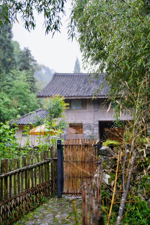 Free Serene view of a rustic countryside house surrounded by lush greenery and bamboo fencing. Stock Photo