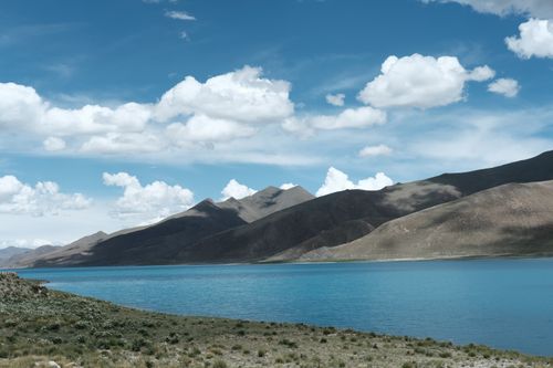 Free Serene mountain landscape with a crystal-clear lake under a vibrant blue sky and fluffy clouds. Stock Photo