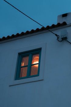 A glowing window on a white building facade in the evening sky.