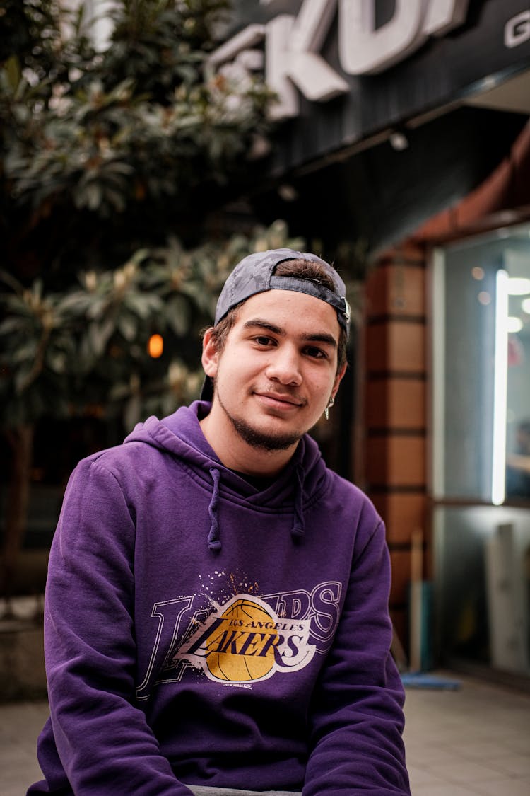 Young Man In A Hoodie And Cap Sitting Outside 