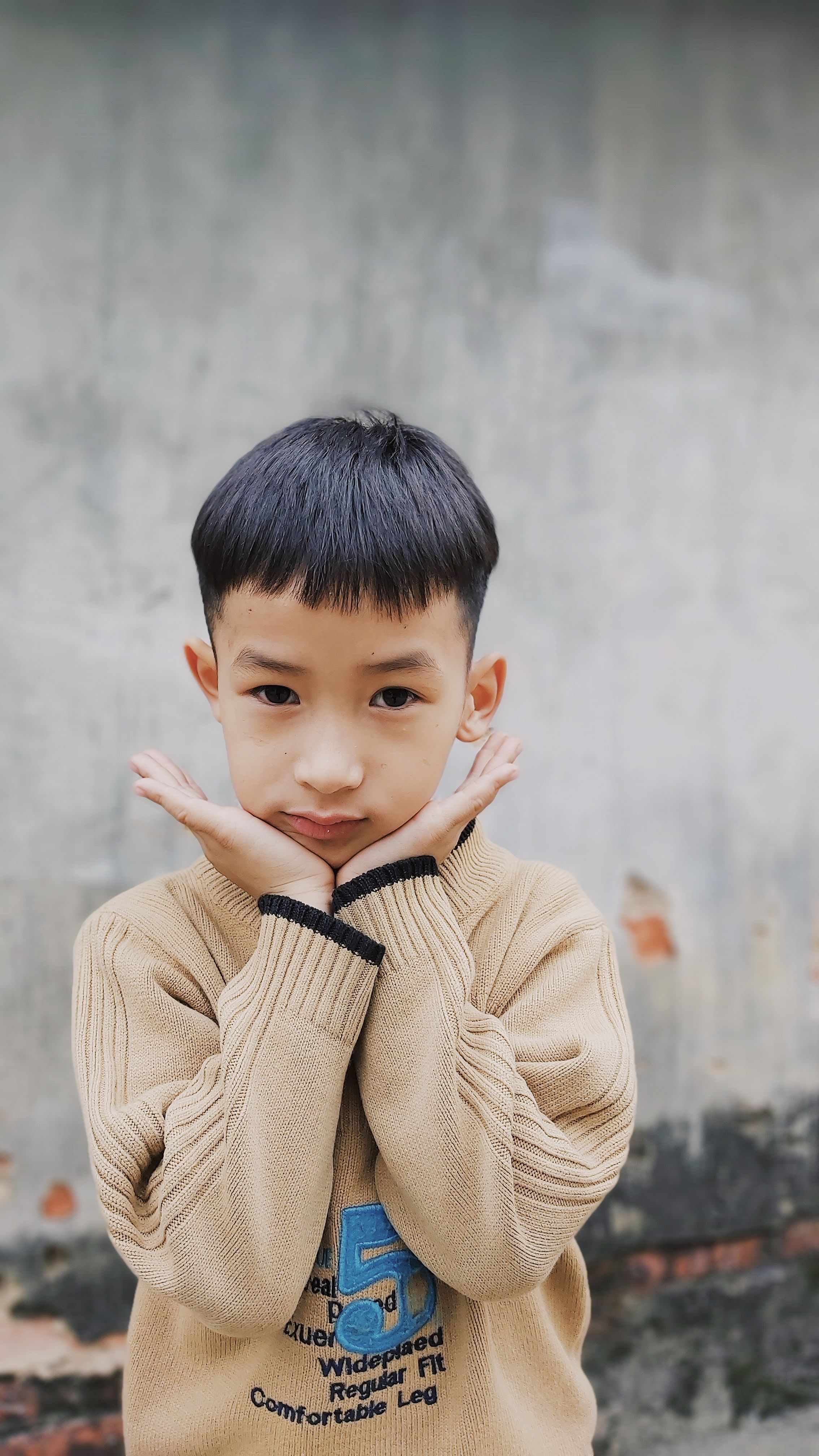 Charming portrait of a young boy posing against a textured wall outdoors, exuding innocence and style.