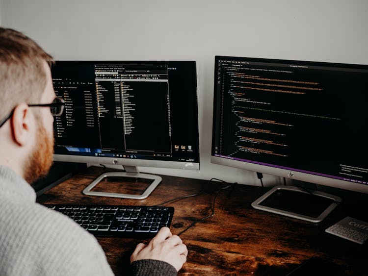 Man Coding On Computers Sitting At Desk