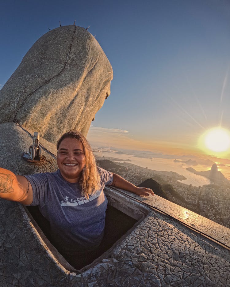 Woman Standing On Top Of The Christ The Redeemer Statue In Rio De Janeiro, Brazil 