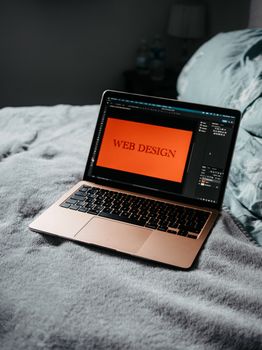 A laptop on a bed showing web design software, creating a cozy workspace.