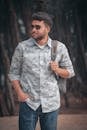 A Man in a Shirt, Jeans and Sunglasses Standing Outside with a Backpack on His Shoulder