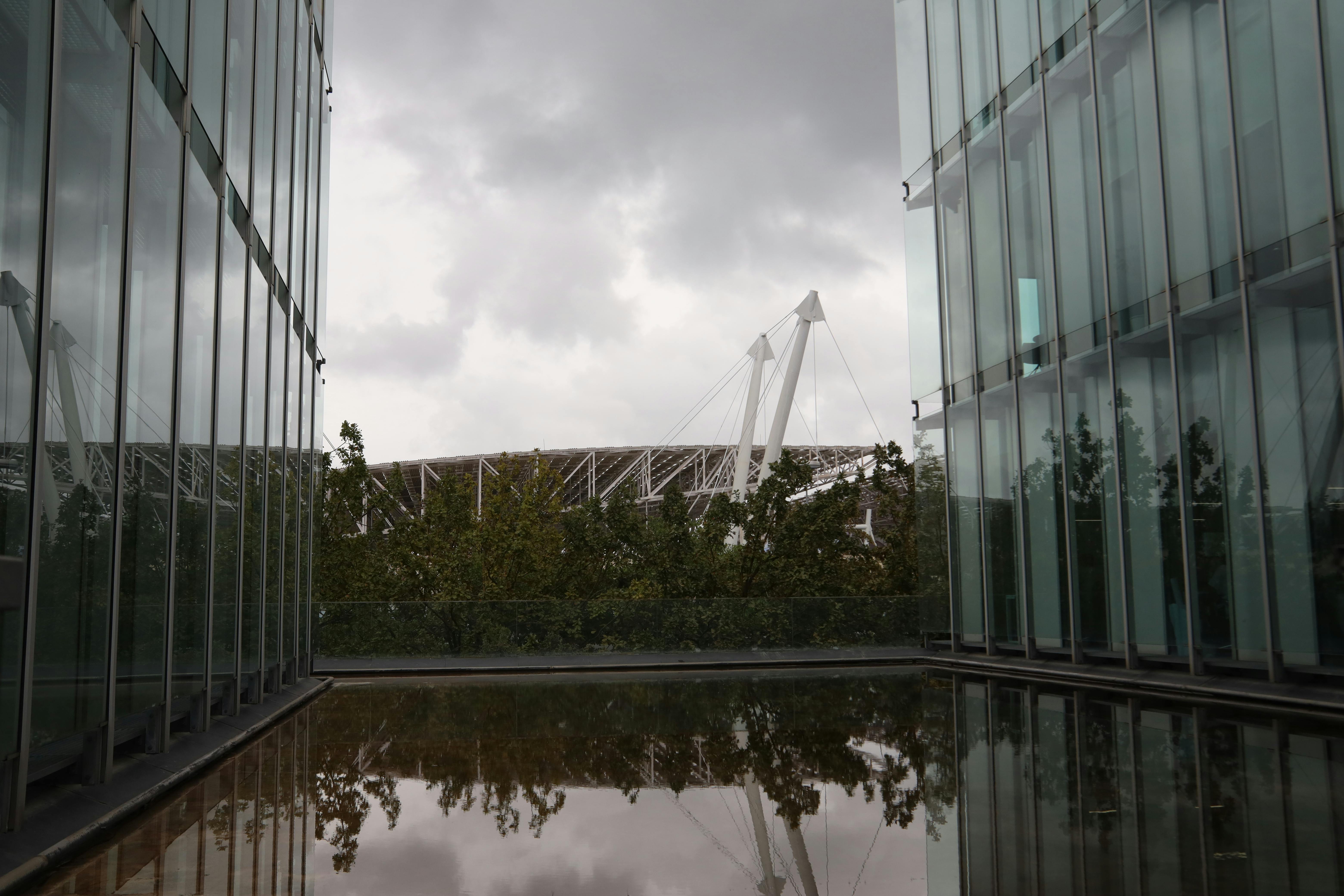 View of a stadium framed by glass buildings and trees under an overcast sky.