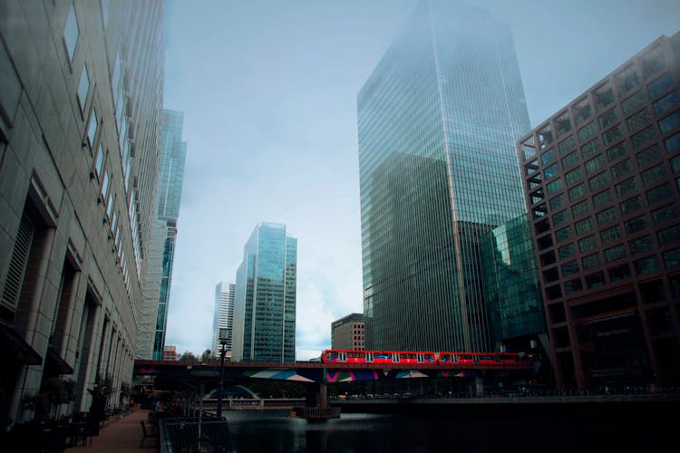 View Of The Train On The Bridge Across The Dock And Next To The 25 Bank Street Skyscraper In Canary Wharf, London, England 