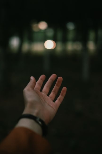 A human hand reaching into a dark, abstract scene lit by soft, blurred night lights.