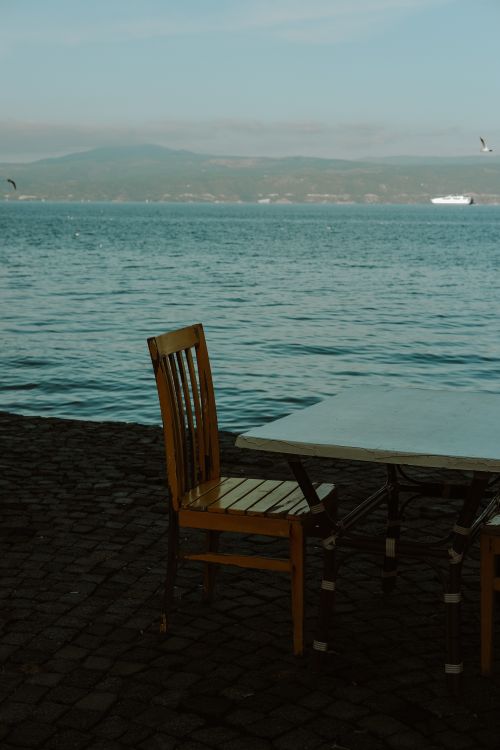 Free Empty wooden table and chair by the sea with distant mountains and a ship in view. Stock Photo