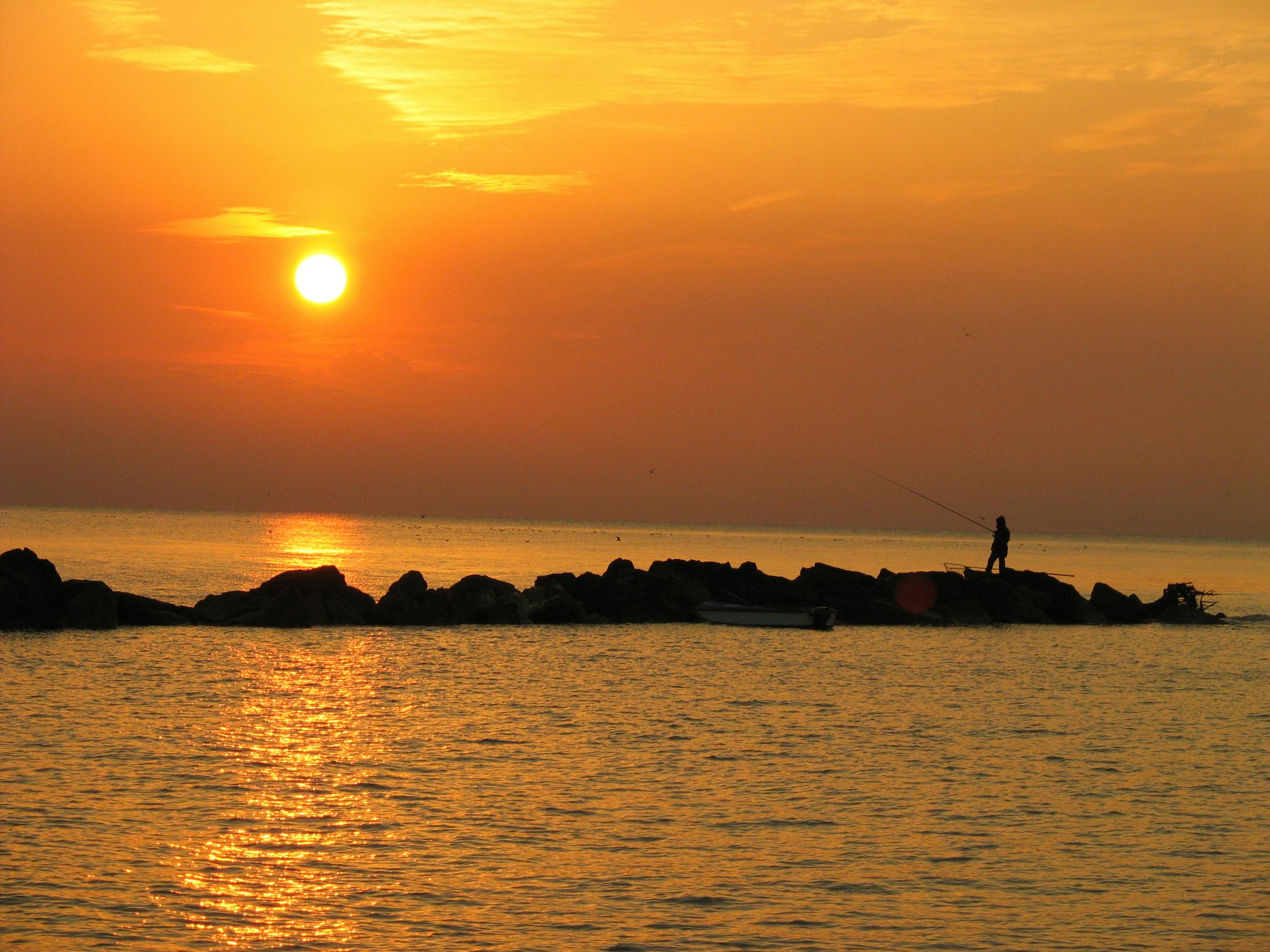 a man fishing at sunset on a rocky shore