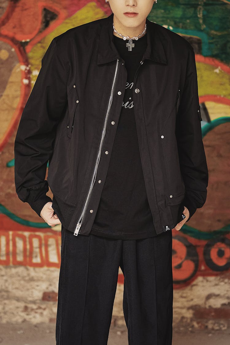 Photo Of A Young Man Wearing A Black Jacket Standing Against A Mural